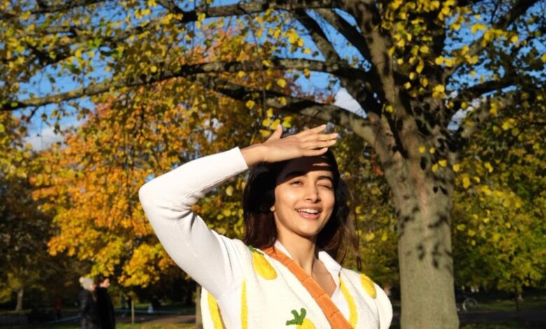 featuring Pooja Hegde, elegantly dressed in a sweater, standing amidst the beauty of a park.