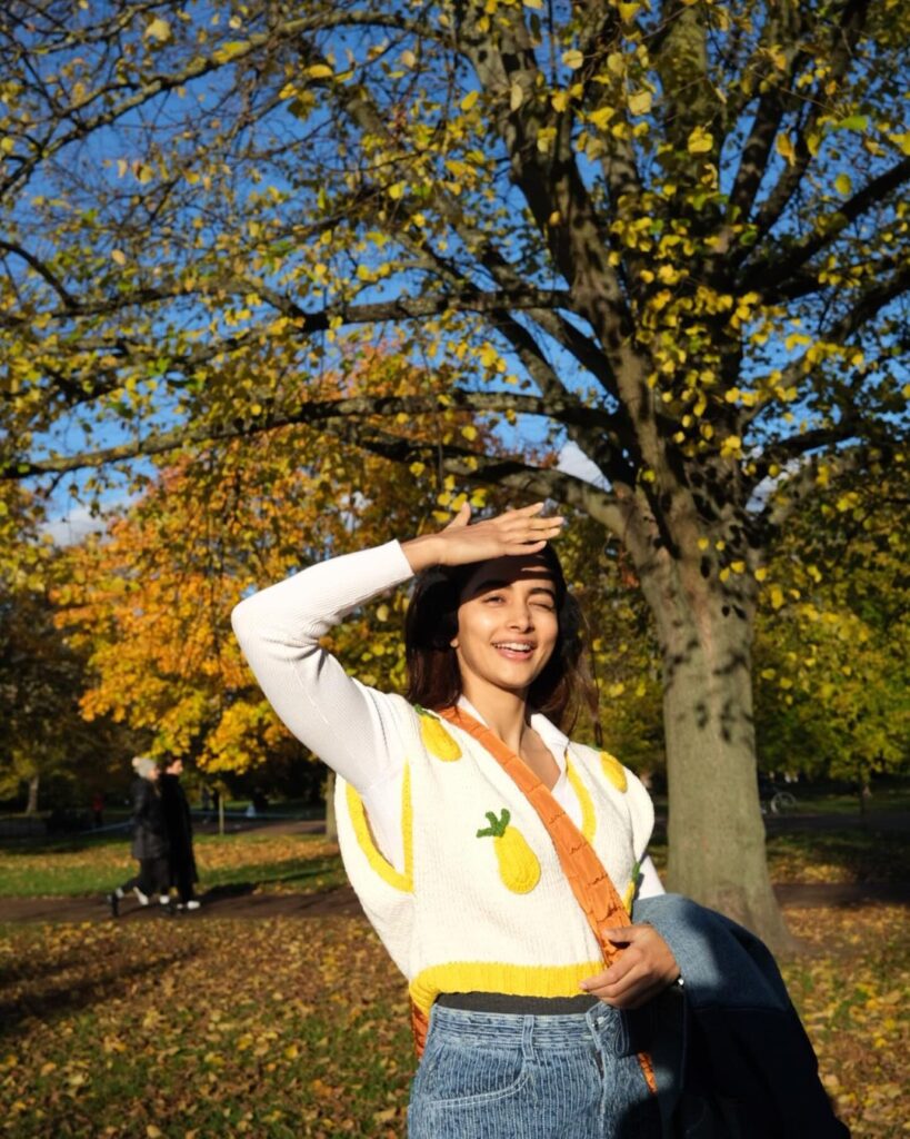 Pooja Hegde in cozy sweater, stands amid scenic park beauty, elegant aura