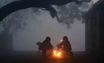 two people sitting around a bonfire under a tree on a winter night.