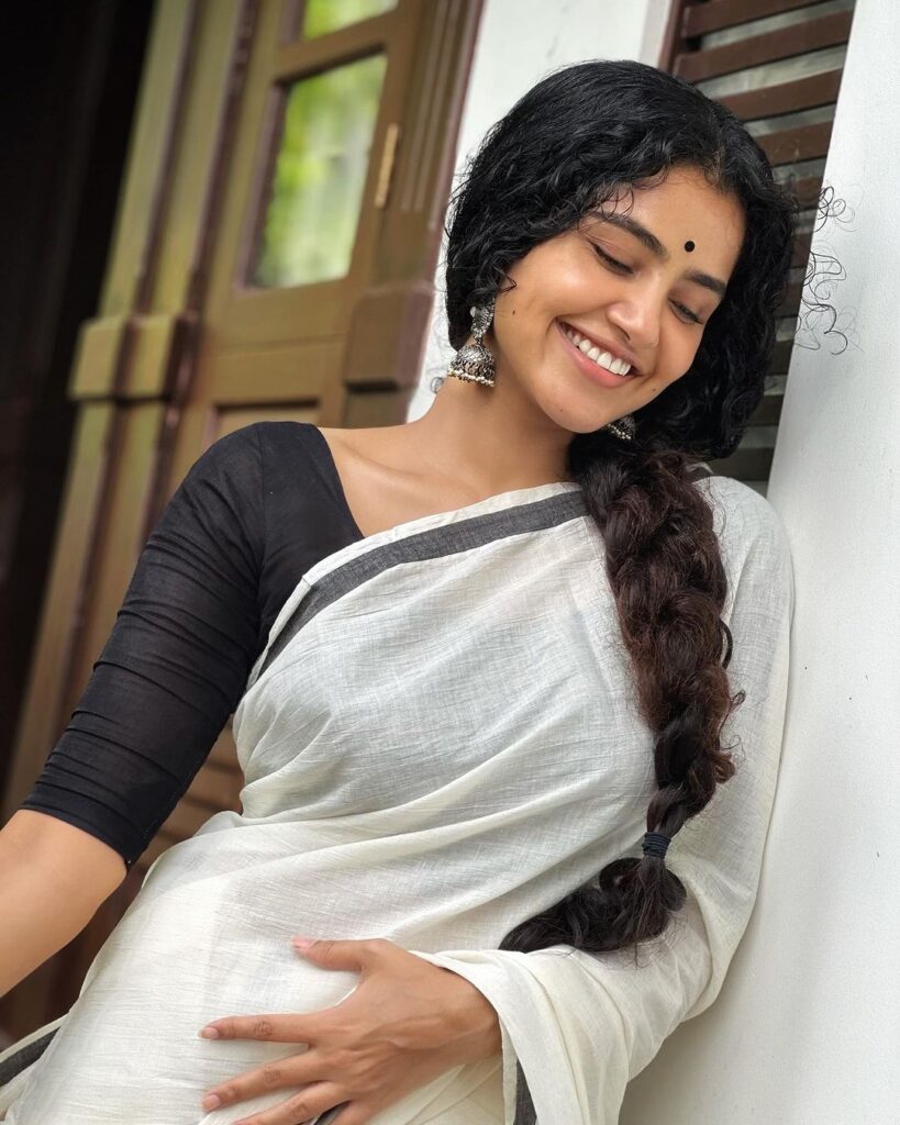 Anupama in white saree and black blouse smiling by looking Downwards